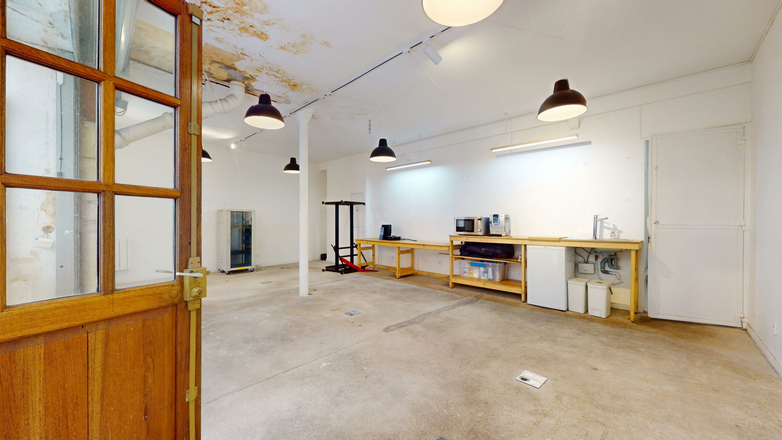Vue depuis la porte vitrée en bois vers le volume principal, traces d'un dégât des eaux au plafond — local commercial 44 m² à louer, rue du Faubourg Saint-Martin, Paris 10e