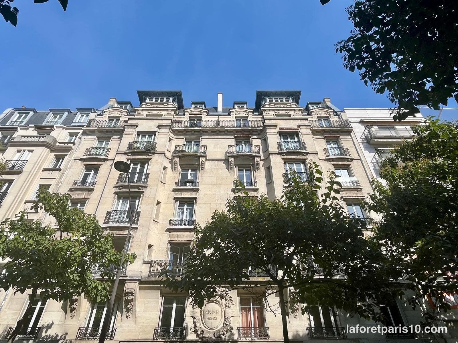 Façade en pierre de taille du 12 avenue de Laumière, Paris 19e, avec toiture mansardée à lucarnes et balcons en ferronnerie