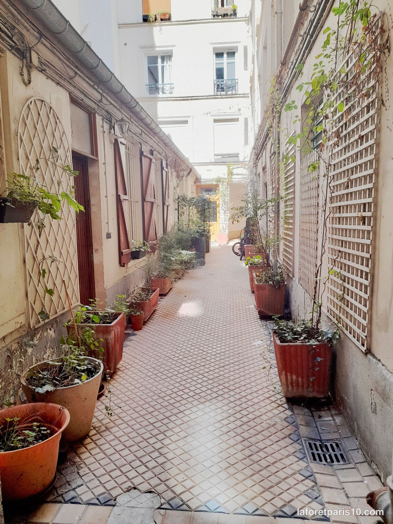 Cour intérieure pavée et plantée du 4 rue de Paradis, Paris 10e, bordée de bâtiments à persiennes