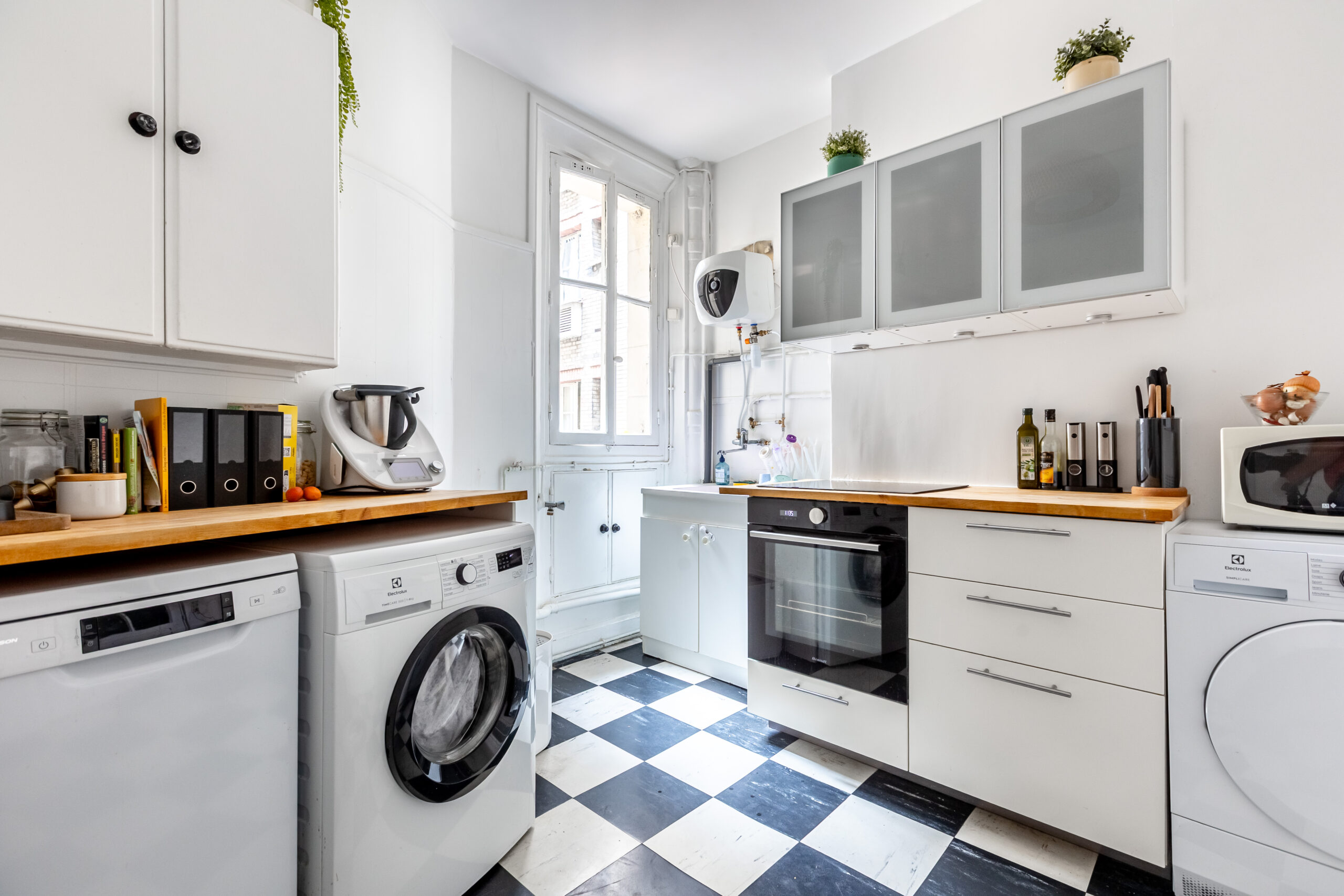 Cuisine indépendante d'un appartement 4 pièces 100,5 m², rue Caulaincourt, Paris 18e : carrelage damier noir et blanc, plan de travail en bois, four et emplacements pour lave-linge et lave-vaisselle