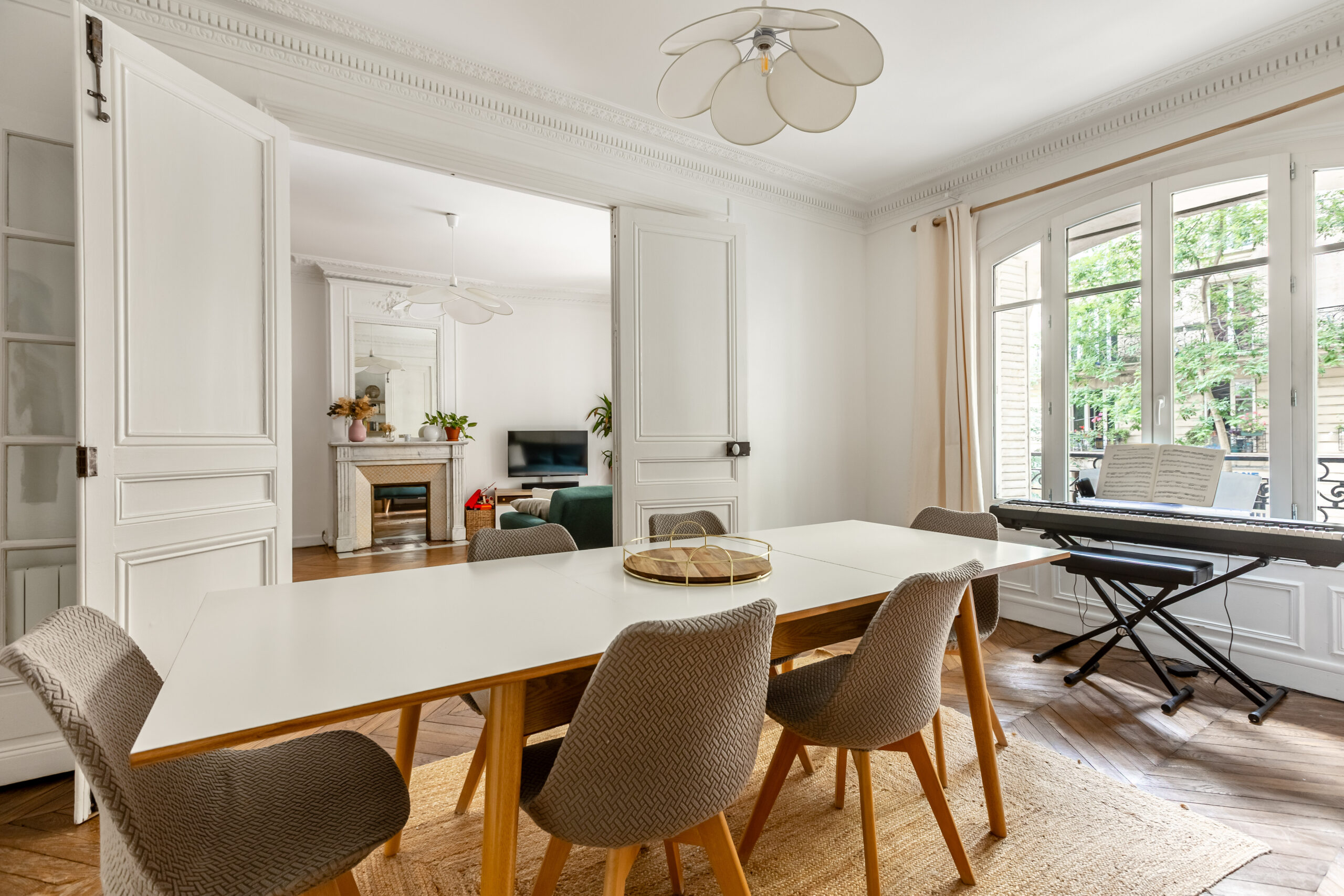 Salle à manger d'un appartement 4 pièces 100,5 m², rue Caulaincourt, Paris 18e, ouverte sur le séjour par une double porte à deux battants, fenêtres côté cour arborée