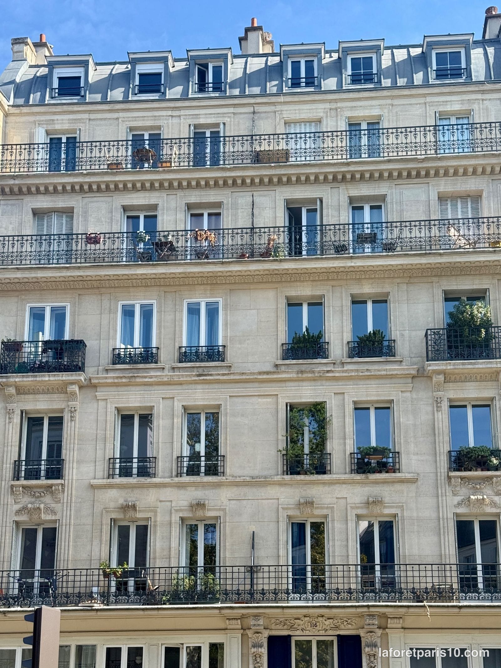 Étages supérieurs du 116 rue du Faubourg Saint-Martin, Paris 10e : balcons filants en fer forgé, corniche et lucarnes