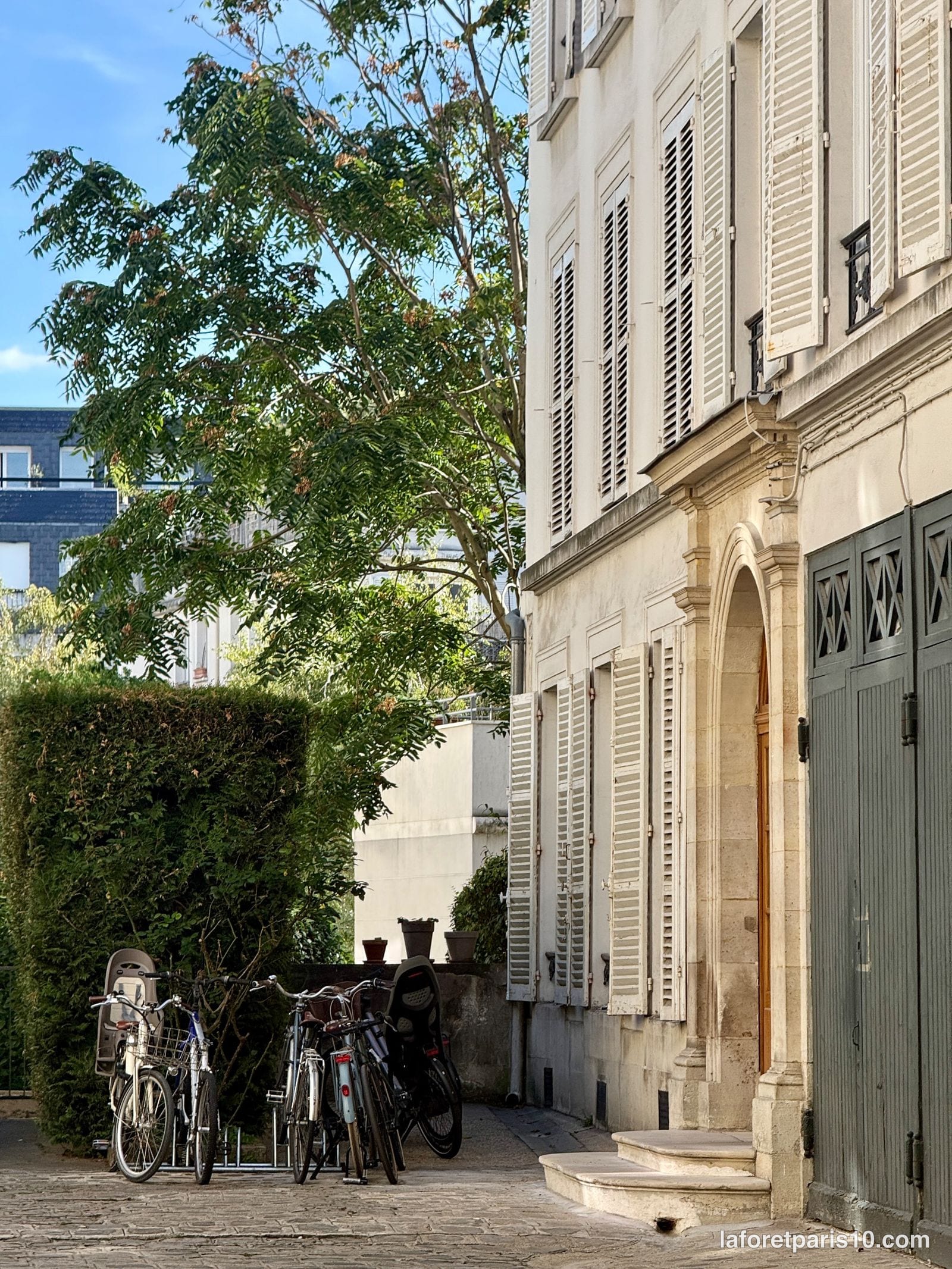 Cour pavée du 188 rue du Faubourg Saint-Martin, Paris 10e : bâtiment à persiennes, porte cintrée à perron et haie