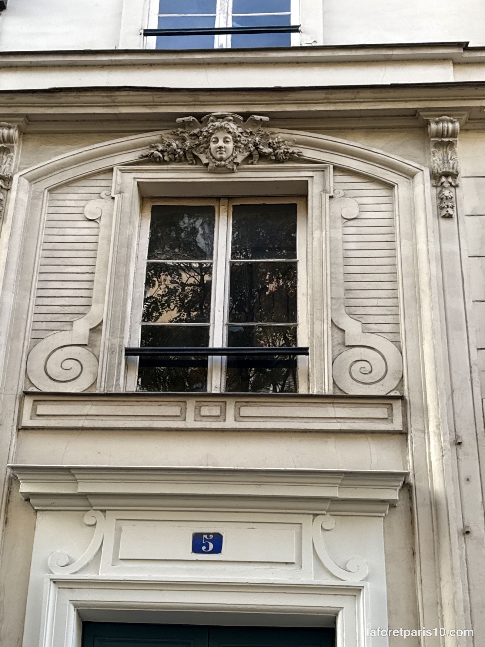 Fenêtre encadrée de volutes sculptées et mascaron au 5 cour des Petites-Écuries, Paris 10e