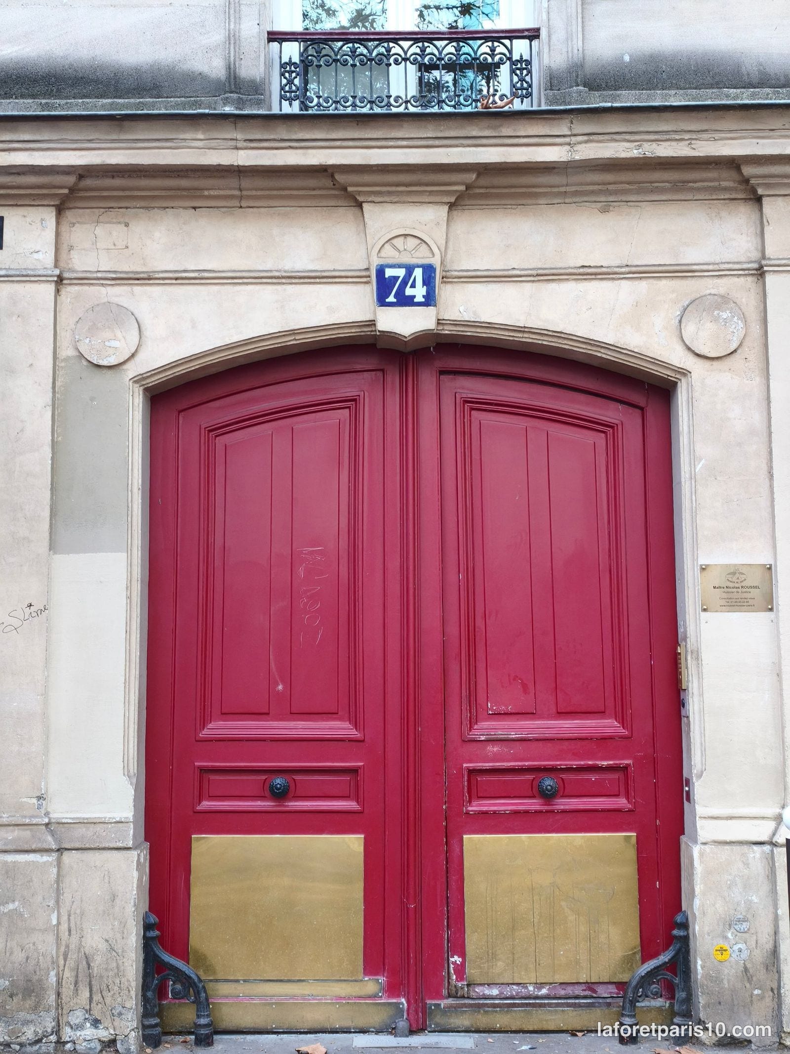 Porte cochère cintrée peinte en rouge du 74 avenue Jean Jaurès, Paris 19e, encadrée de deux médaillons de pierre