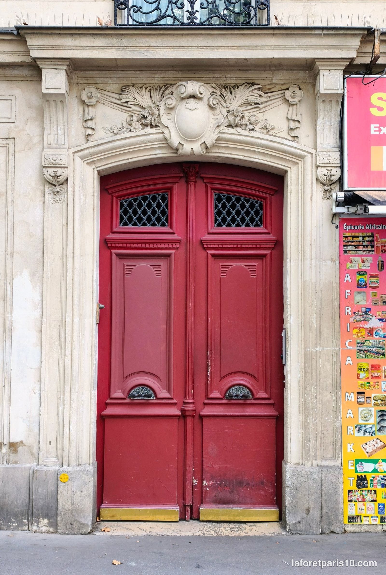 Porte cochère rouge du 76 avenue Jean Jaurès, Paris 19e, sous un cartouche sculpté de palmes